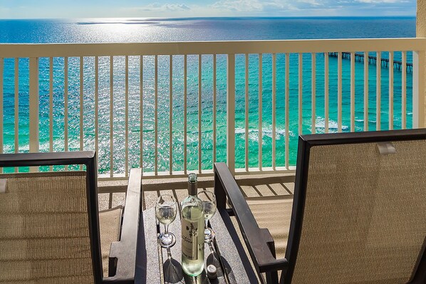 A balcony with a view of turquoise waters and a pier in the distance.