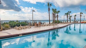 Ein Pool mit klarem, blauem Wasser, umgeben von Liegestühlen und Tischen, mit Blick auf den Ozean und einen Steg im Hintergrund.
