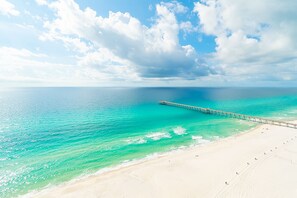Una playa con un muelle largo que se extiende hacia el mar turquesa, bajo un cielo parcialmente nublado.