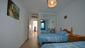 Quarto com duas camas, mesa de cabeceira de madeira, espelho e um quadro na parede.