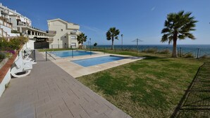 Uma área de piscina com duas piscinas, um gramado e vista para o mar.