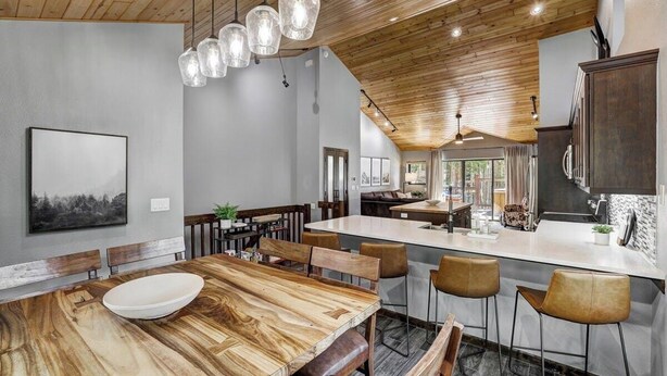 A modern kitchen with a large island, wooden dining table, and pendant lighting.