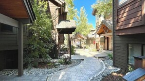 A courtyard with wooden buildings, a stone pathway, and greenery.