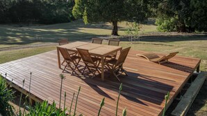 A wooden deck with a table and chairs, surrounded by a grassy area and trees.