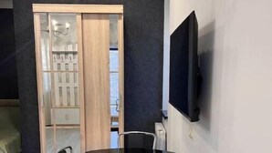 A compact living space with a glass dining table and chairs, a TV mounted on the wall, and a sliding door leading to a storage area. - House in Antarayin, Yerevan, Armenia (Yerevan)