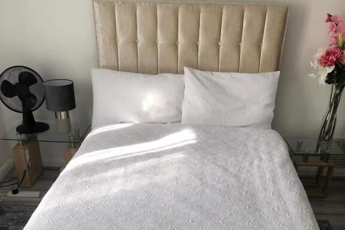 A neatly made bed with a tufted headboard, white linens, and a simple bedside table with a lamp.
