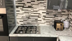 A kitchen with a gas stove, a toaster, and a coffee maker on the countertop. - Featherstone Court (London)