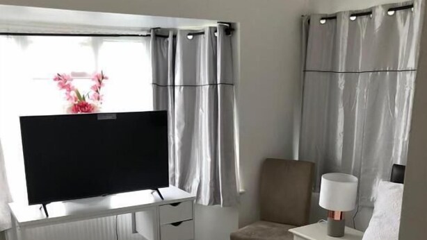 A hotel room with a bed, a desk with a TV, a chair, a nightstand with a lamp, and curtains. - Featherstone Court (London)