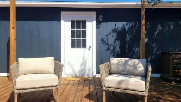 Two wicker chairs with white cushions on a wooden deck, a white door, and a dark blue wall. - Silver pine one bedroom with a nice patio deck. (Austin)