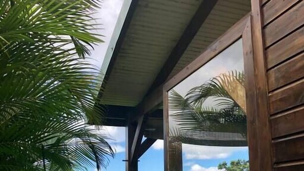 En træbygning med en overdækket terrasse, omgivet af frodig vegetation og udsigt til fjerne bakker.