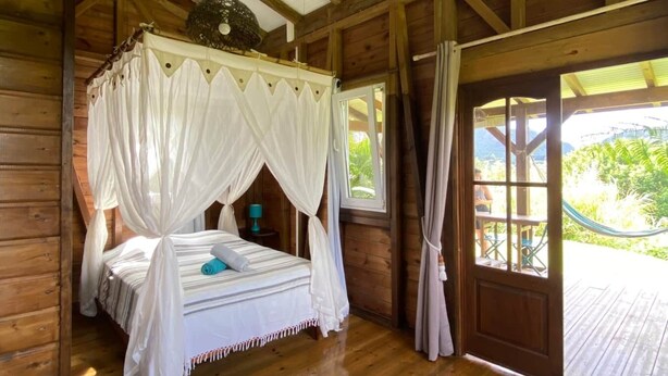 A wooden cabin with a four-poster bed, a hammock, and a view of greenery outside. - Bungalow on a mountainside (Le Morne Rouge)