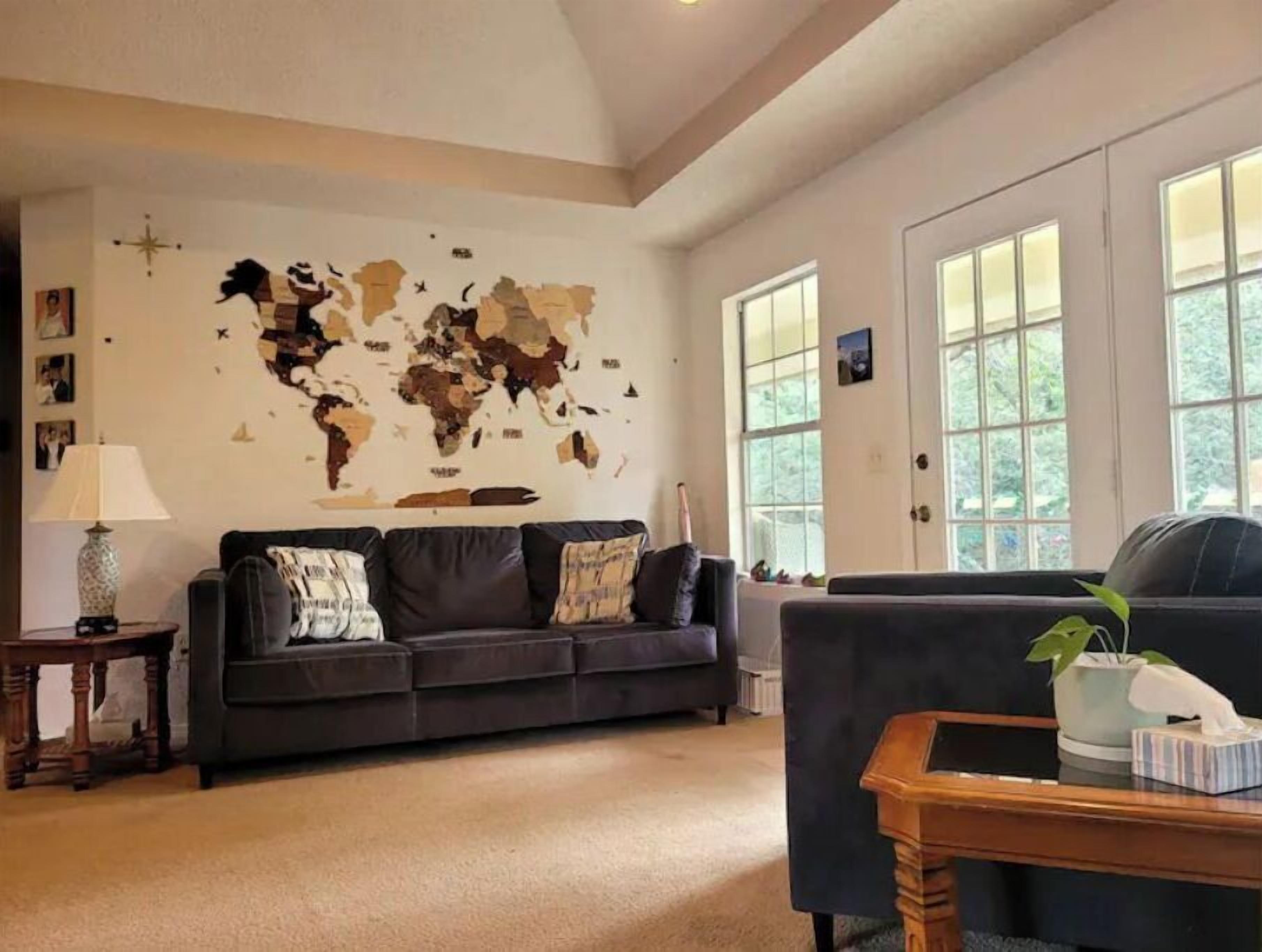 A living room with a large world map on the wall, a dark-colored sofa, a wooden coffee table, and large windows.