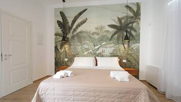 Una camera da letto con un letto grande, biancheria bianca, un murale tropicale sulla parete e una porta a sinistra.