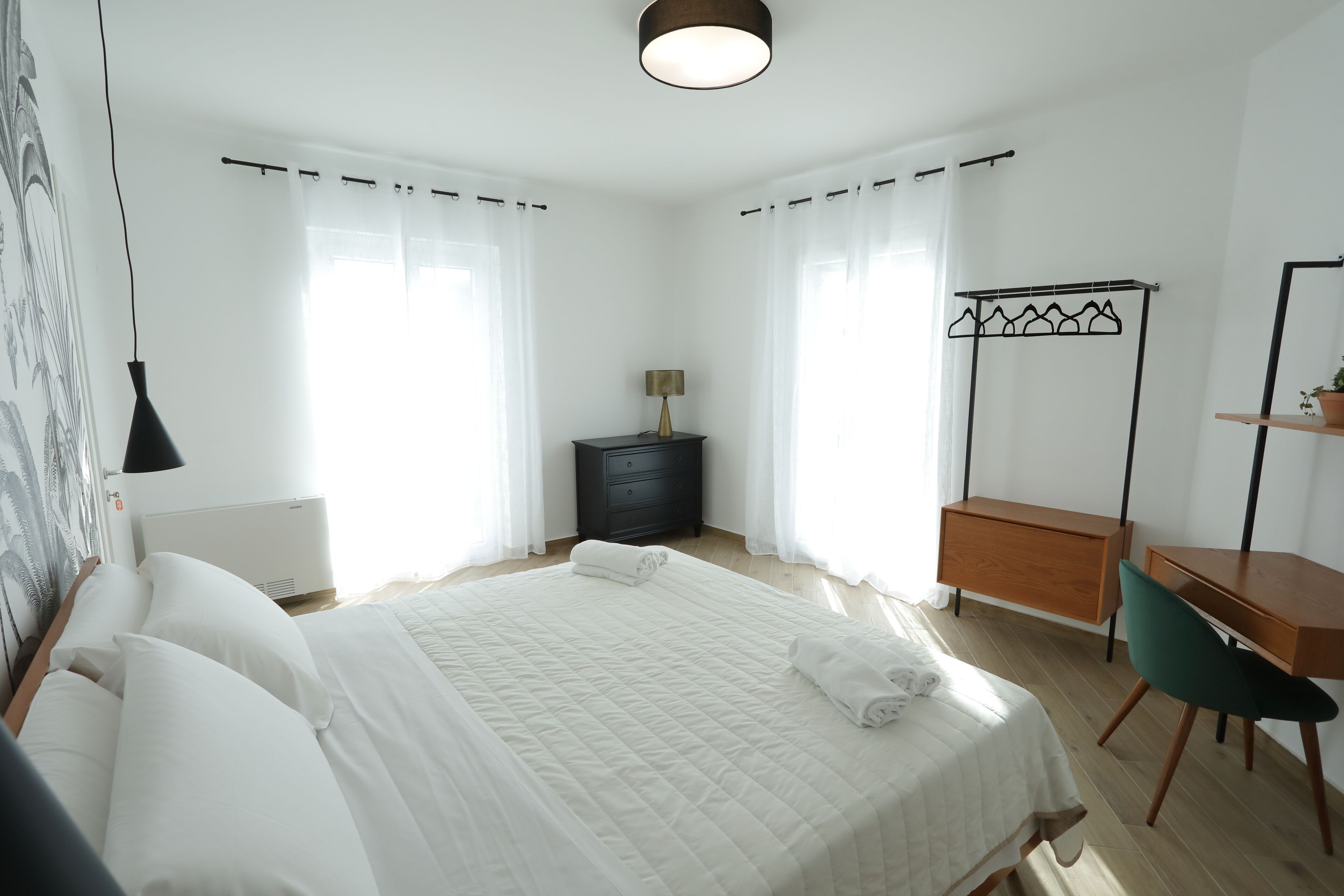 Ein ordentlich eingerichtetes Schlafzimmer mit Bett, Nachttisch, Lampe und Schreibtisch mit Stuhl.