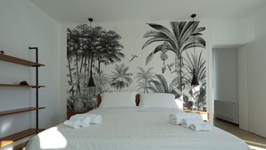 Een slaapkamer met een groot bed, witte beddengoed en een tropische muurschildering.
