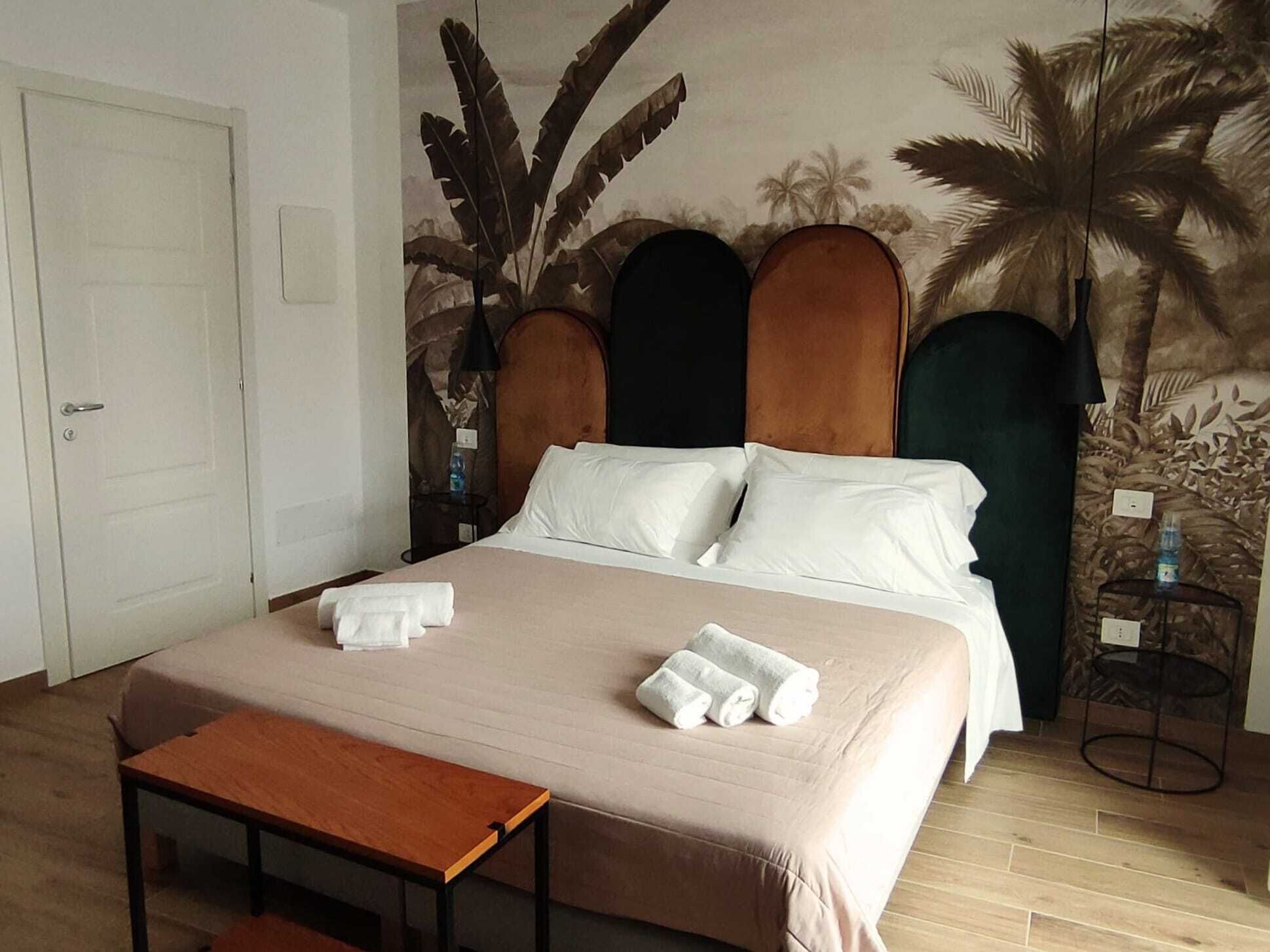 A hotel room with a bed, a wooden nightstand, a small table, and a door.