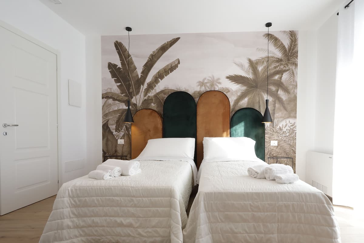 Een hotelkamer met twee bedden, een tropische muurschildering en een witte deur.