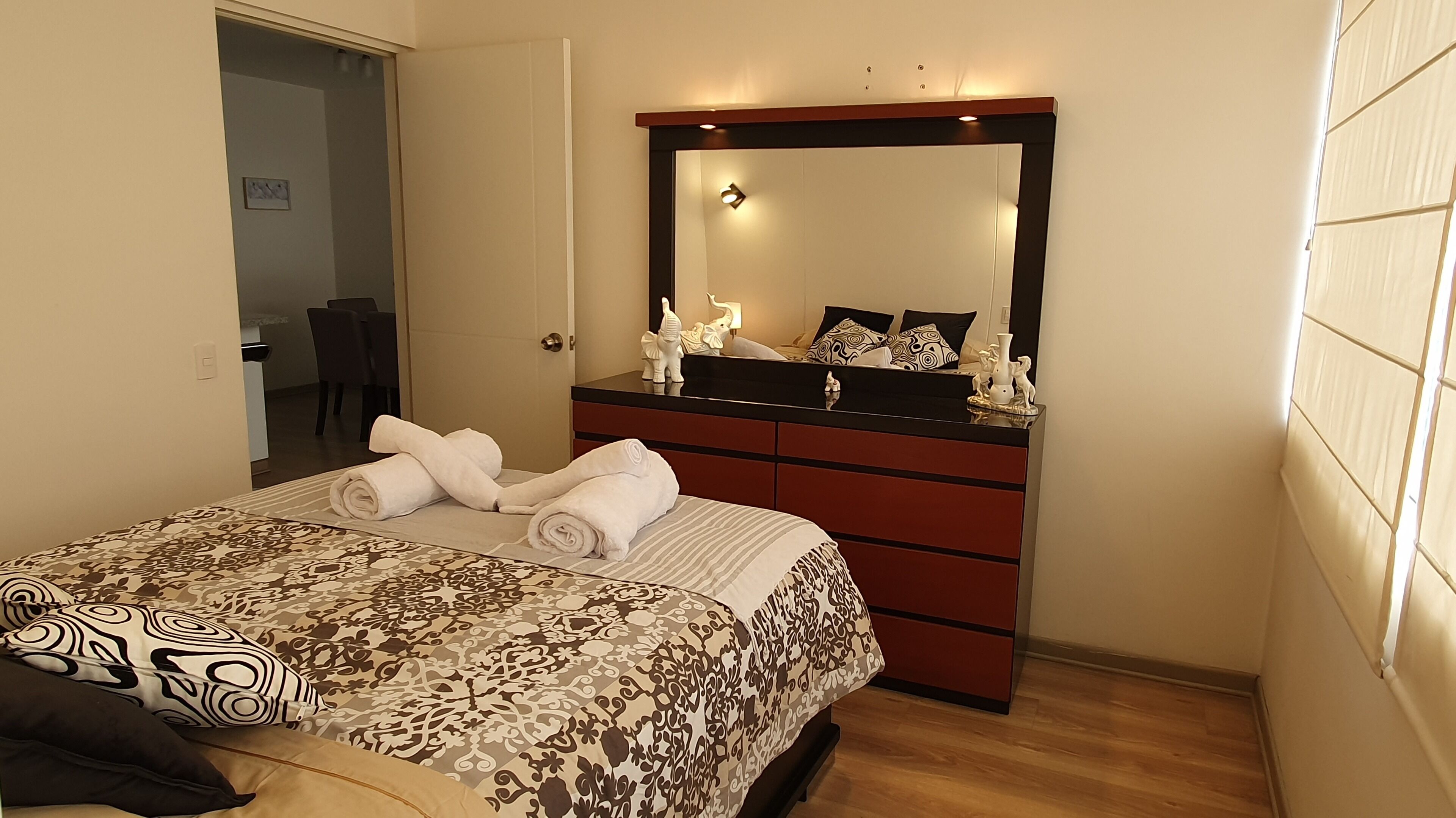 Un lit bien fait, avec des serviettes pliées, une commode avec un miroir et une couvre-lit à motifs.