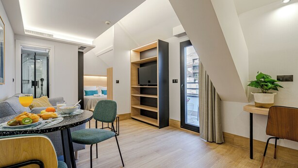 A modern dining area with a table set for breakfast, a sofa, and a bookshelf. - Feelathome Ventas Suites (Madrid)