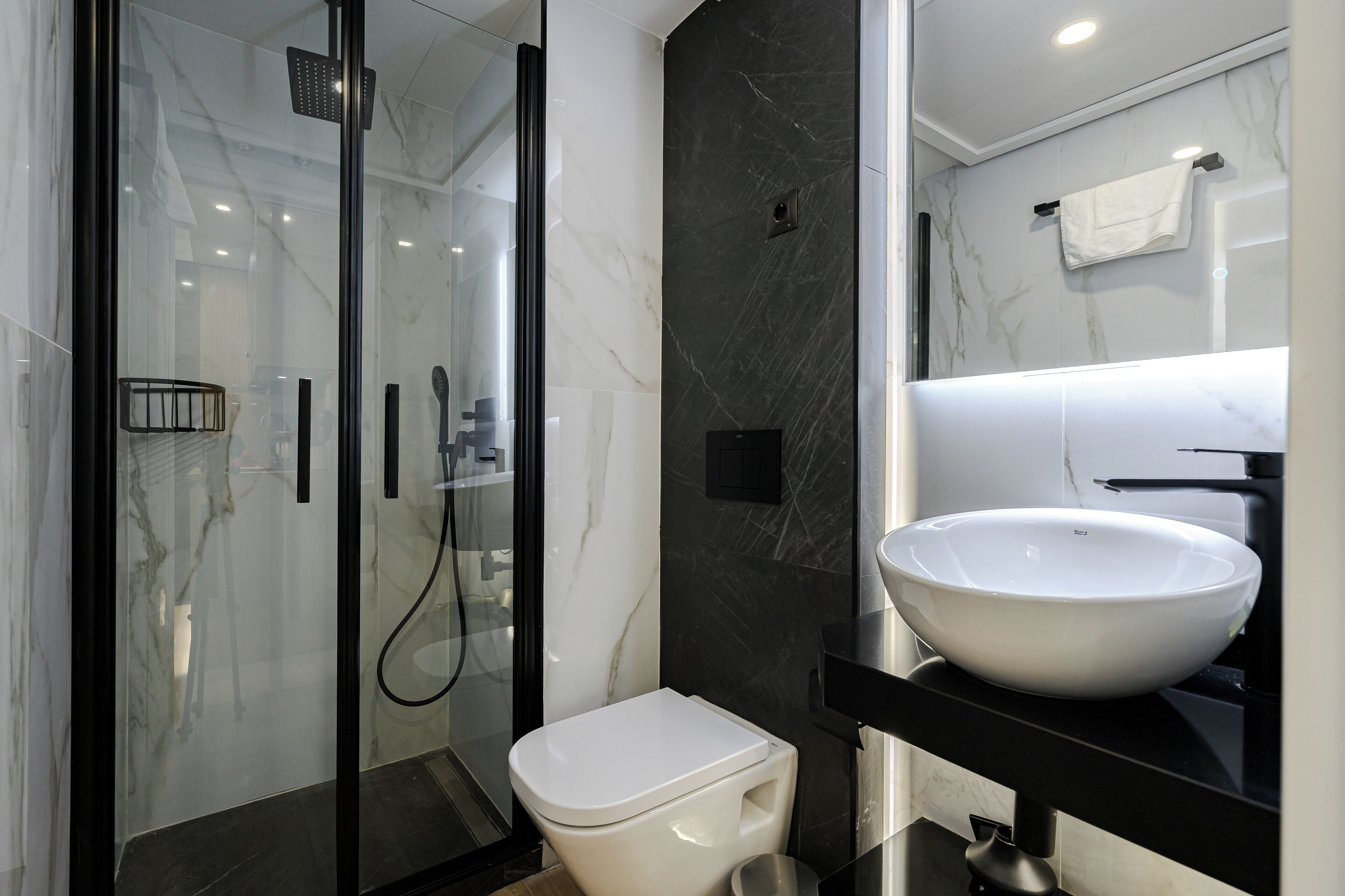 Een moderne badkamer met een douchecabine van glas, een wit toilet en een grote witte wastafel op een zwart aanrecht.