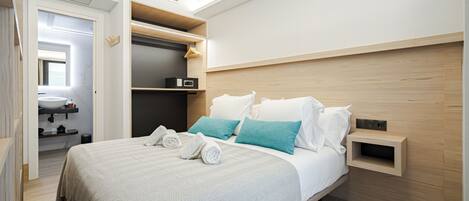 A modern hotel room with a large bed, a built-in wardrobe, a bedside table, and a small shelf.