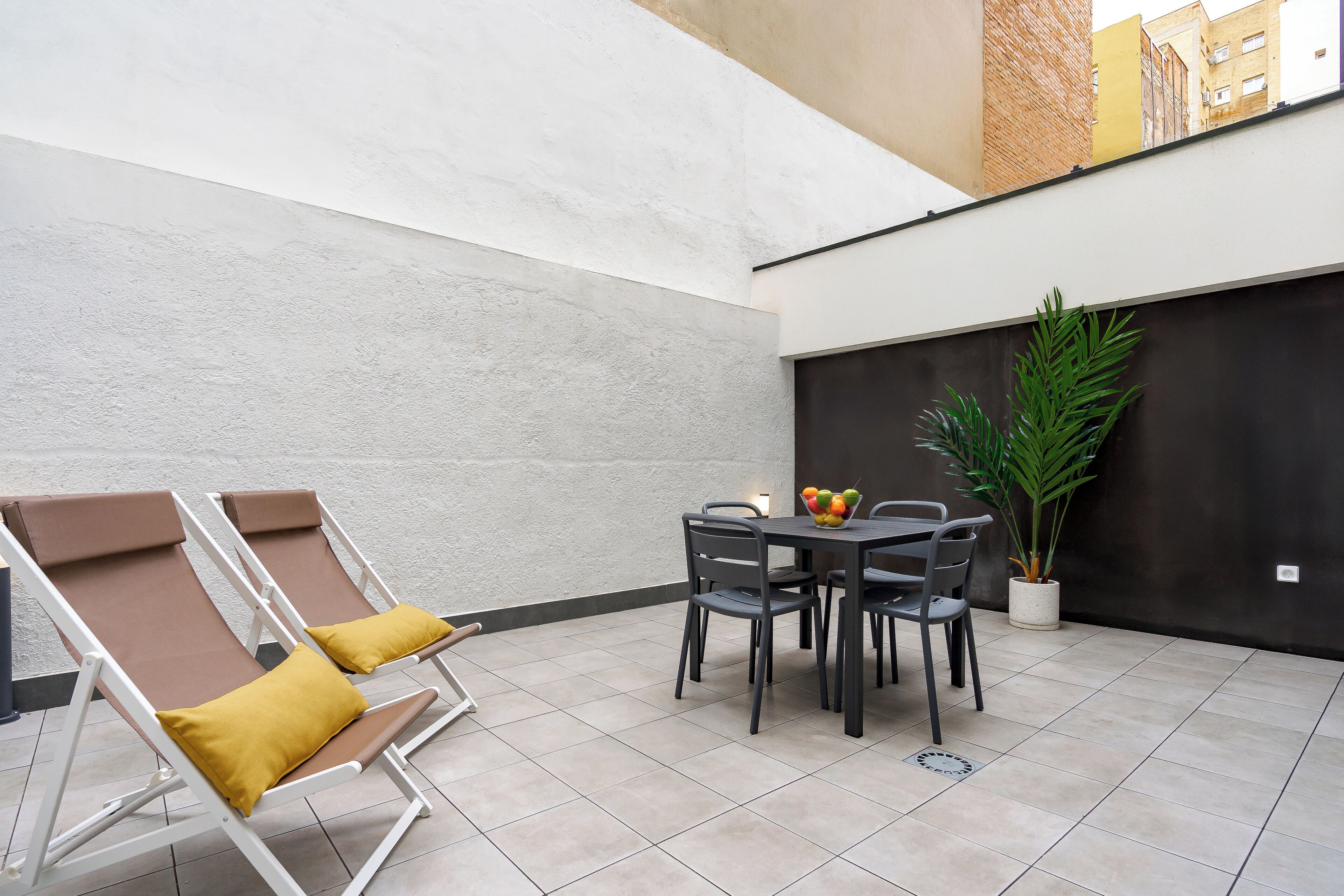 Een terrasgedeelte met twee loungestoelen, een tafel met stoelen en een bloempot.