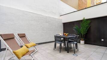 Een terrasgedeelte met twee loungestoelen, een tafel met stoelen en een bloempot.