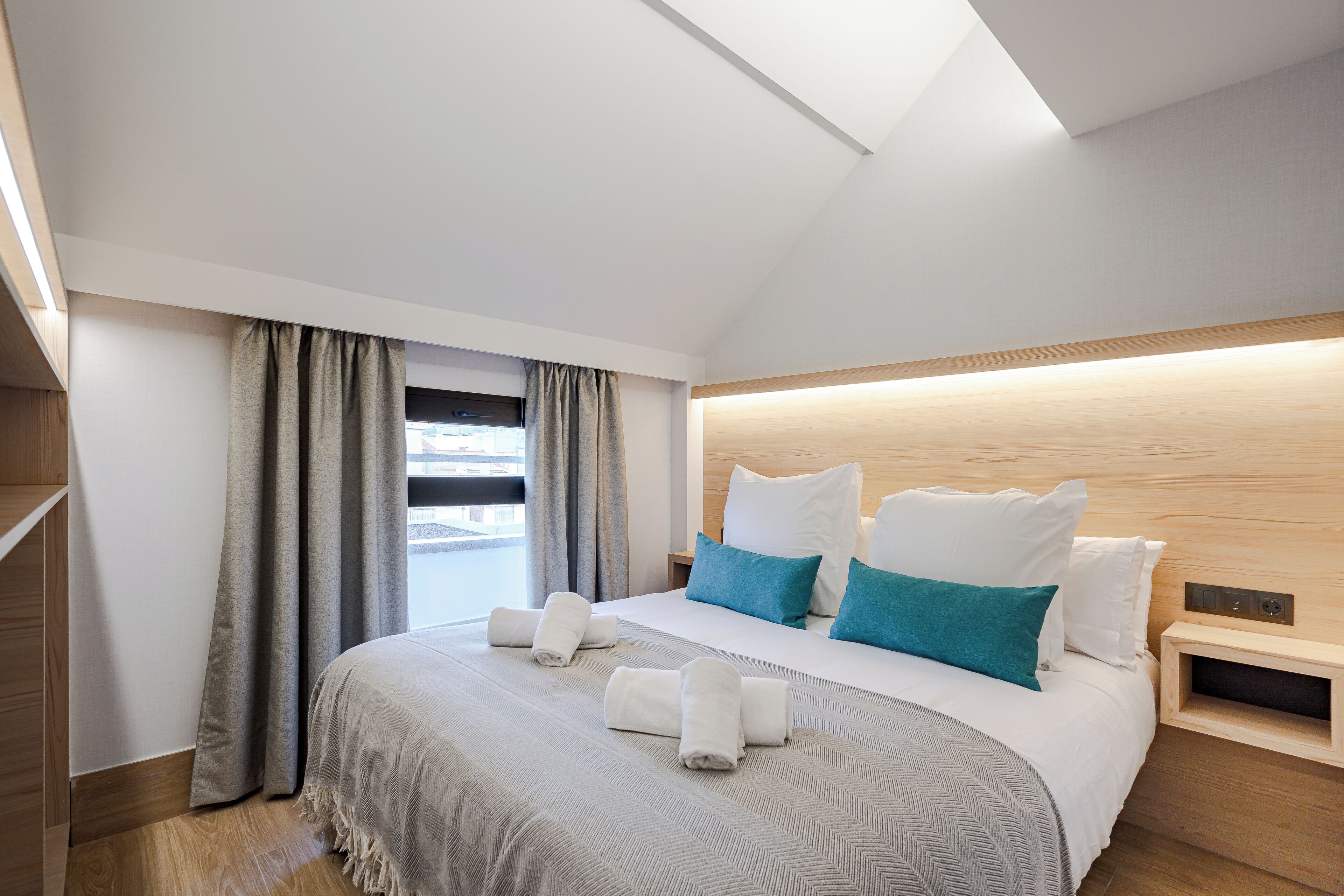 Una habitación de hotel moderna con una cama grande, cabecero de madera y vistas a la ciudad.