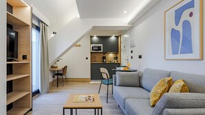A modern living room with a grey sofa, a wooden coffee table, and a dining area with a small table and chairs. - Feelathome Ventas Suites (Madrid)