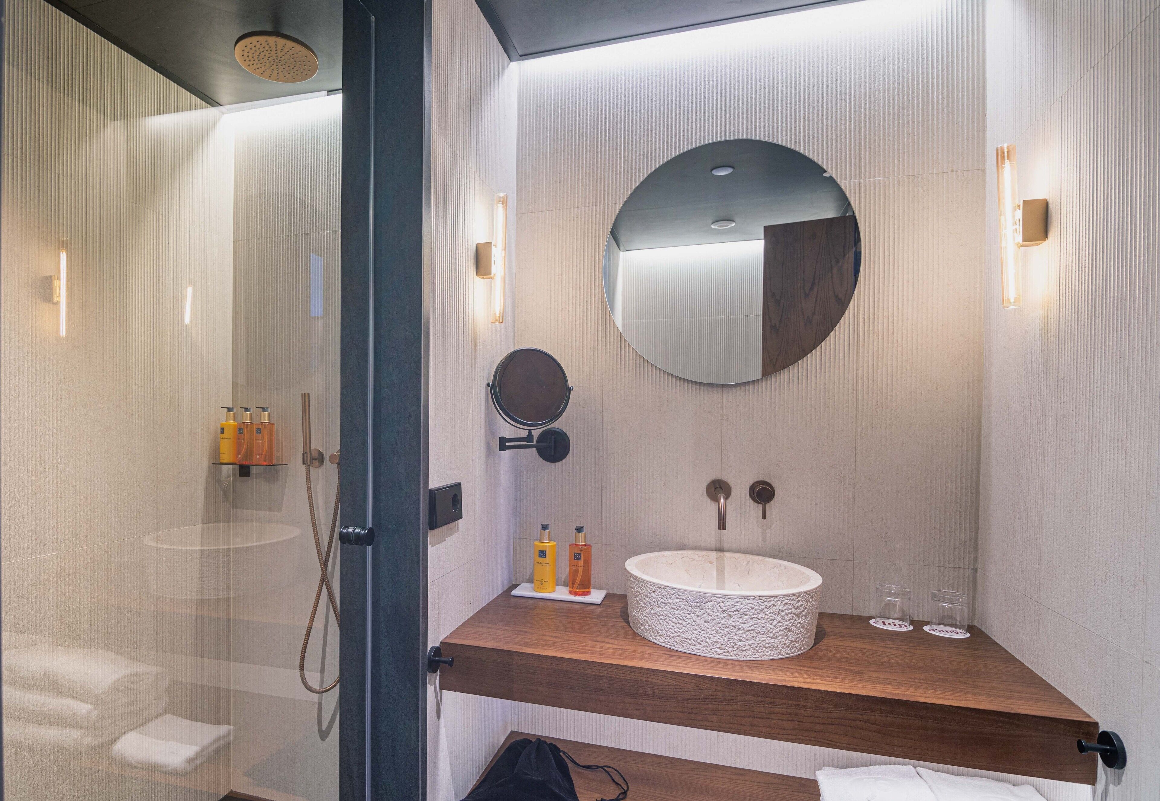 Une salle de bain moderne avec un grand miroir rond, un plan de toilette en bois et une douche à parois de verre.