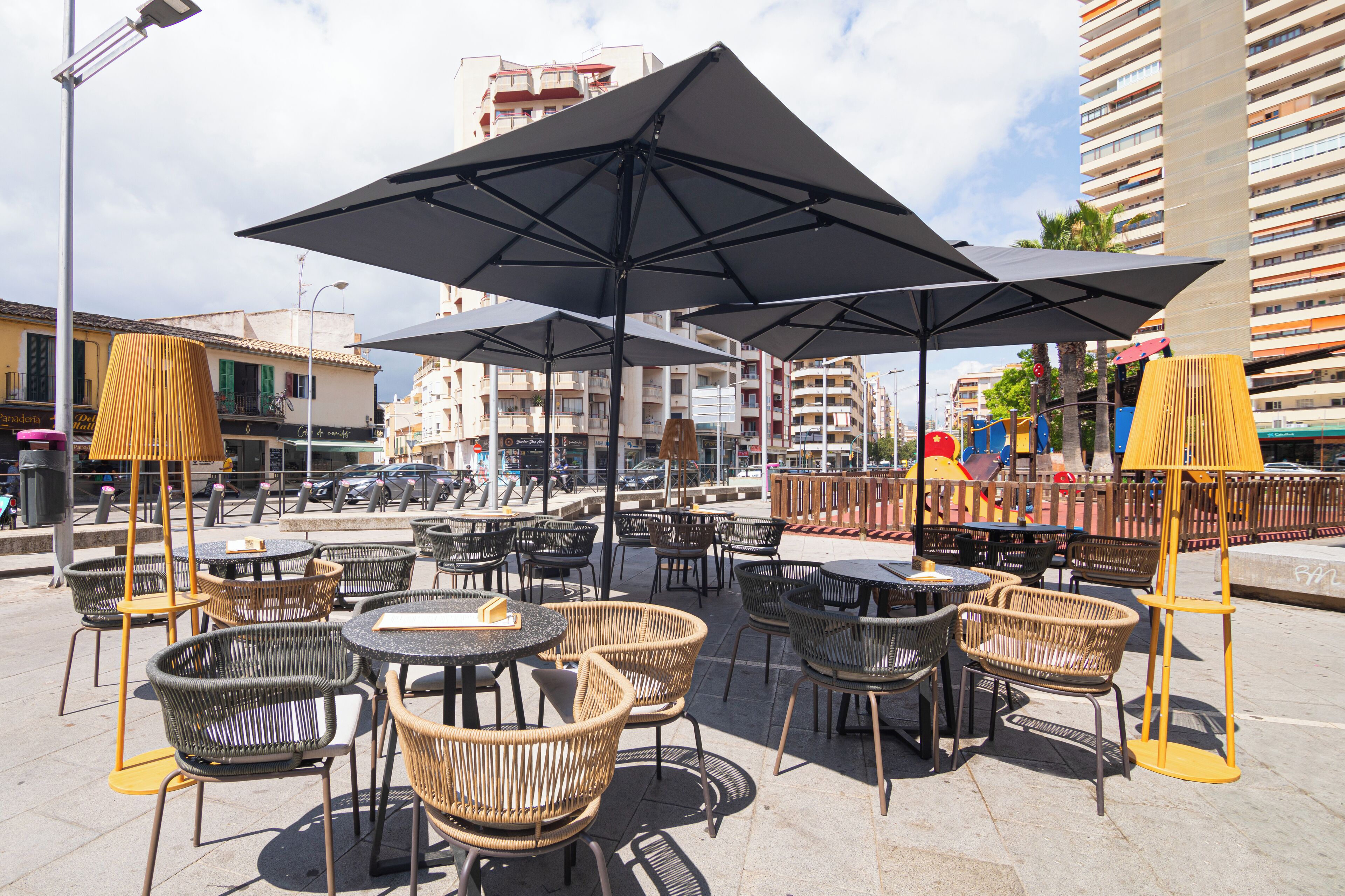 Terrassensitzgelegenheiten mit Tischen und Stühlen, Sonnenschirmen und Blick auf die Straße mit Gebäuden und Autos.