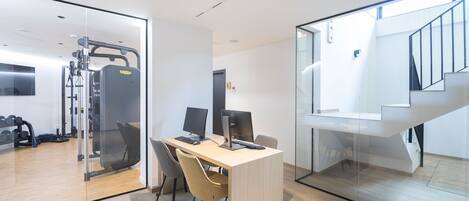 A modern office space with a desk, computers, and a gym area visible through glass partitions.