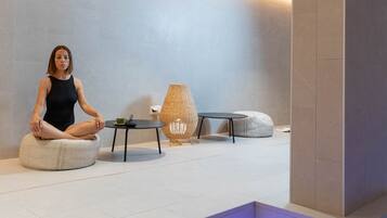 A modern spa area with a person meditating on a bean bag, a small table with a cup, and a decorative lamp.