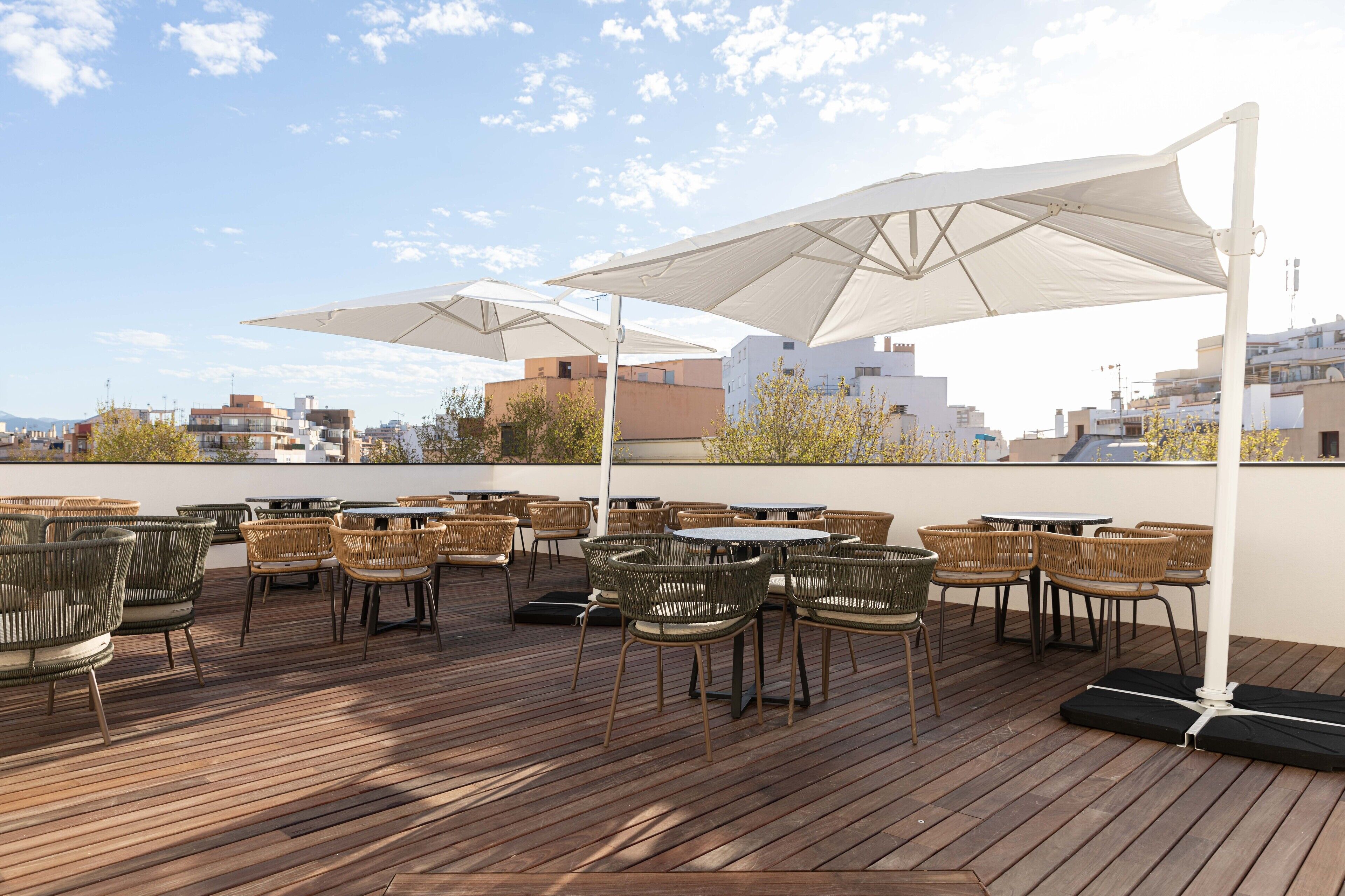 A rooftop terrace with wooden flooring, wicker chairs, and large umbrellas providing shade.
