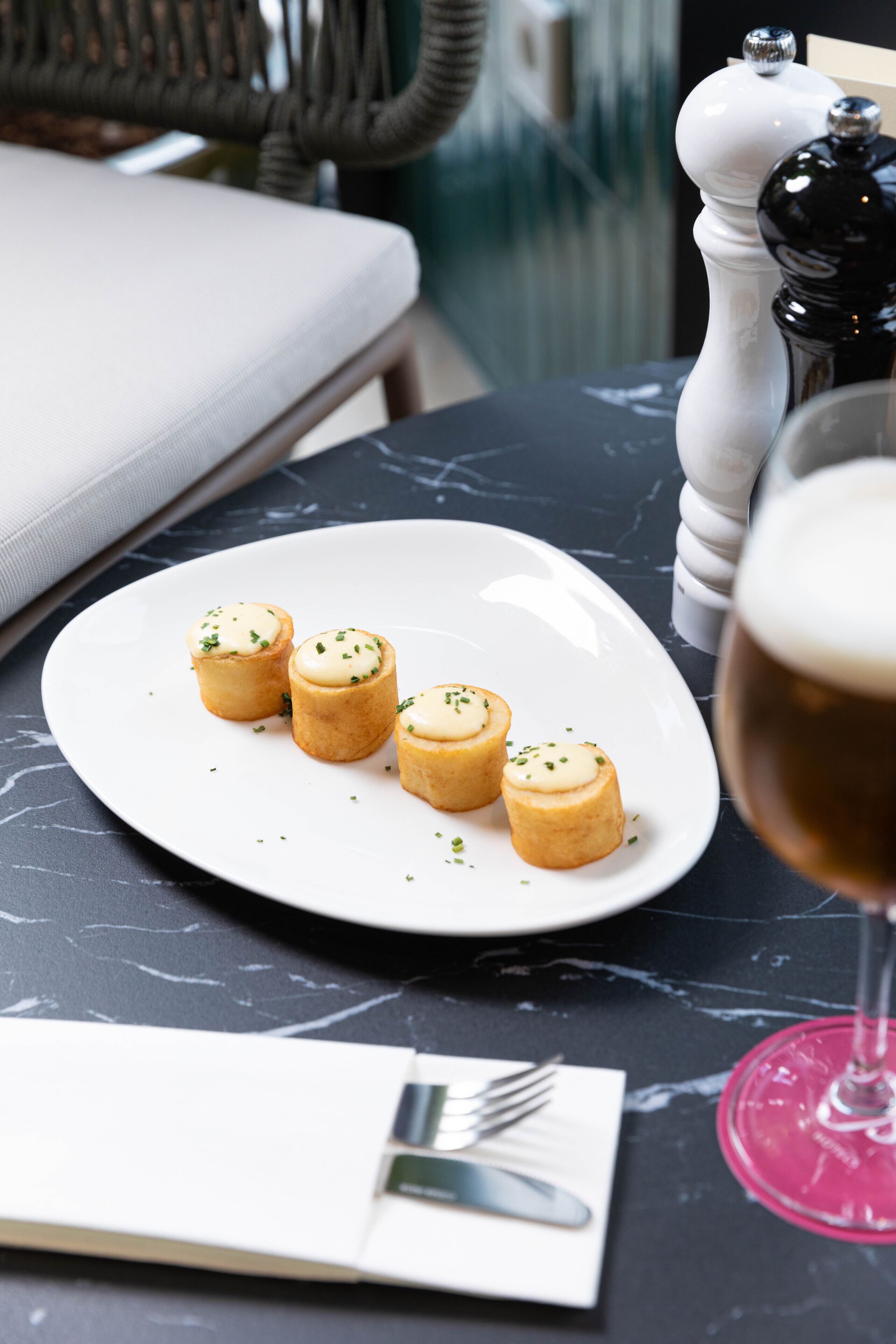 Ein Esstisch mit einer Platte Mini-Quiches, einem Salz- und Pfefferstreuer, einem Weinglas und einer Gabel auf einem Servietttuch.