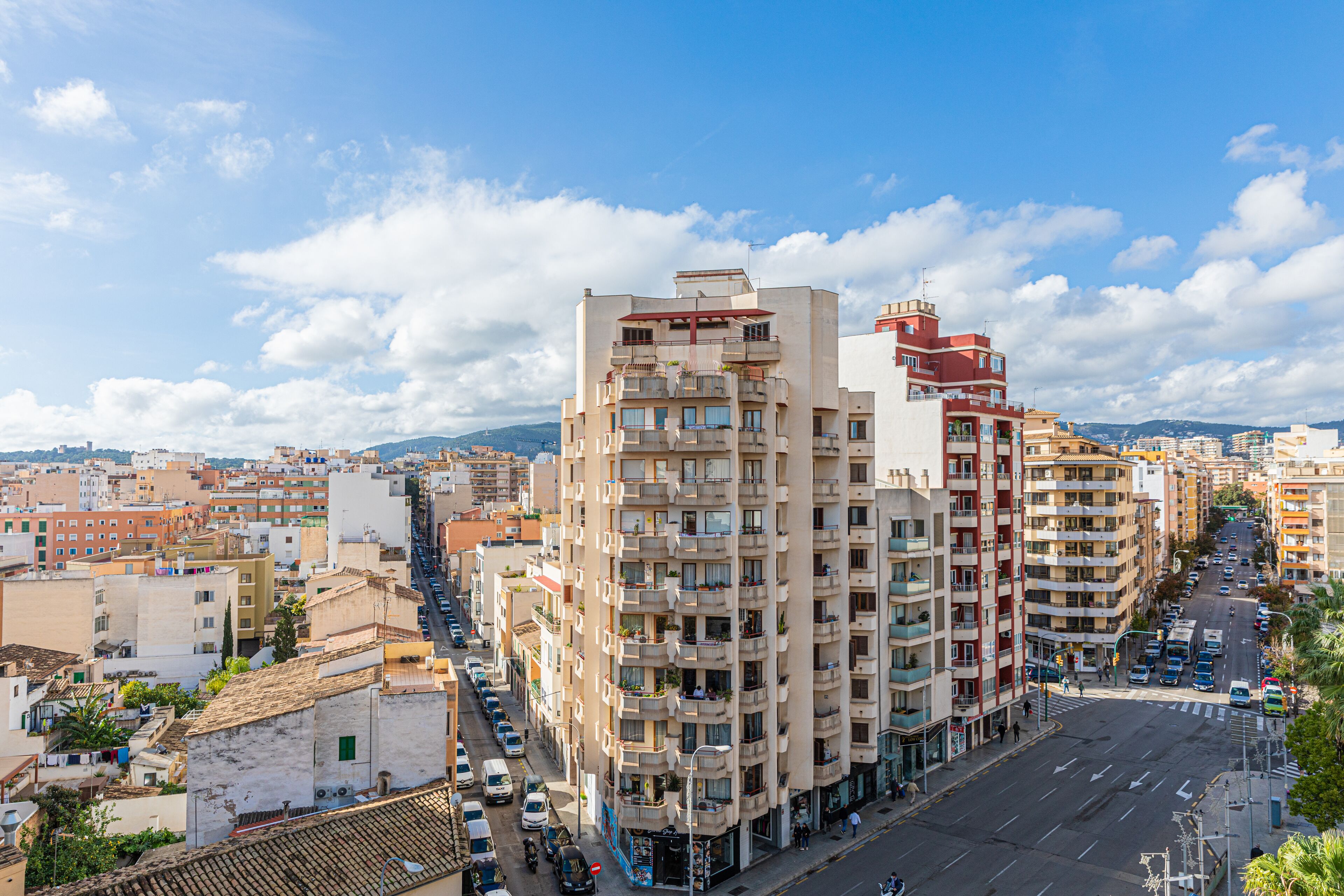 Un edificio de varios pisos con balcones, una calle frente a él y un cielo despejado.
