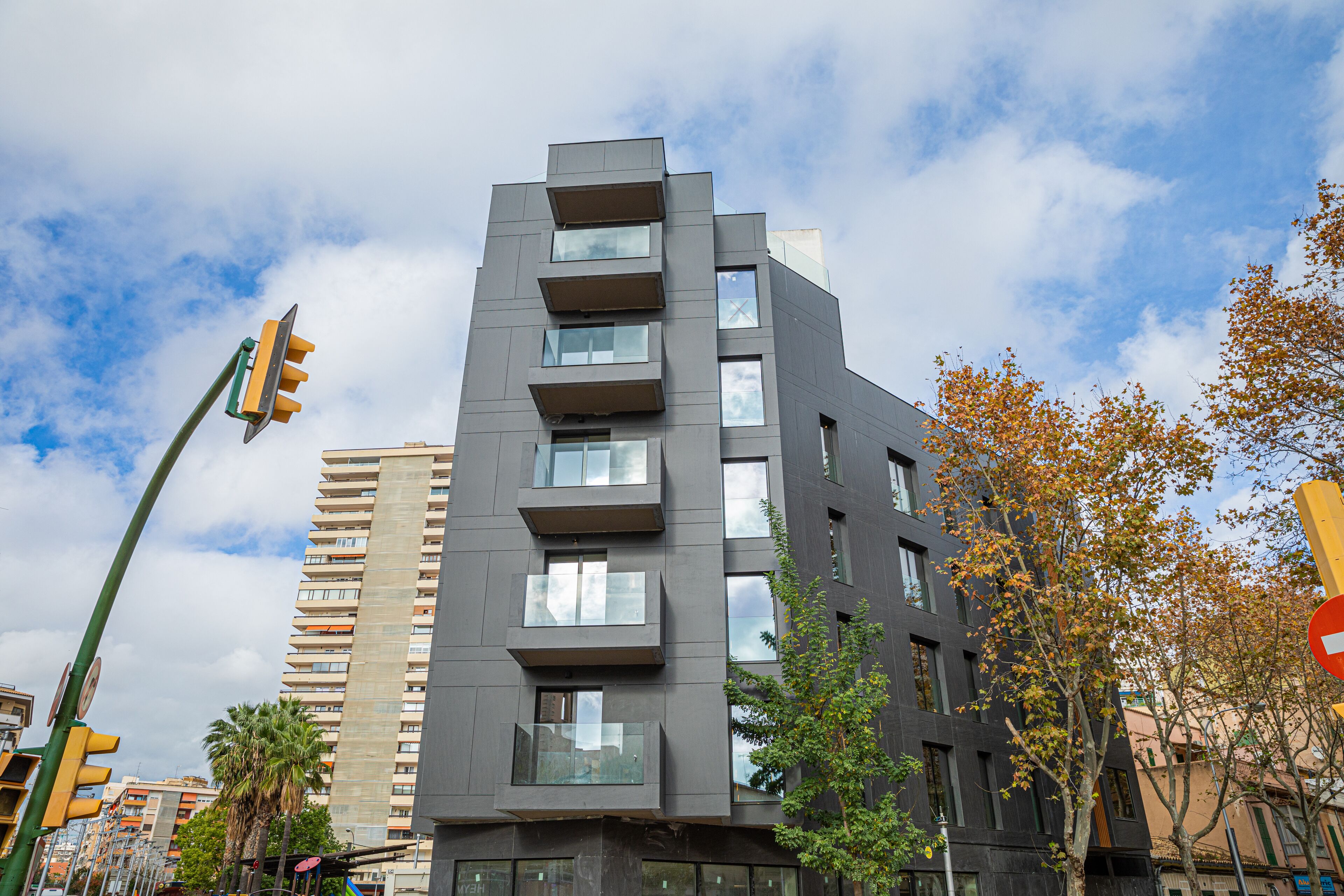A modern multi-story building with balconies, large windows, and a street view with traffic lights.