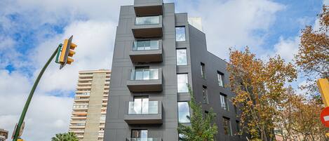 A modern multi-story building with balconies, large windows, and a street view with traffic lights.