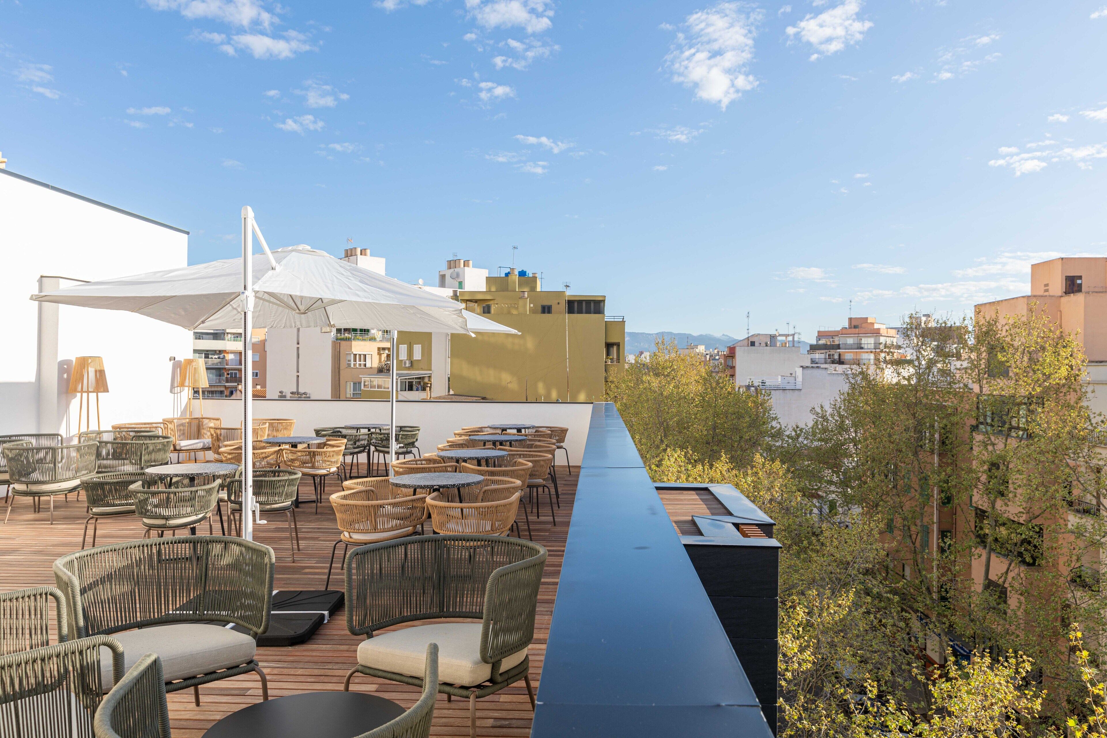 A rooftop terrace with wicker furniture and umbrellas, overlooking a cityscape.