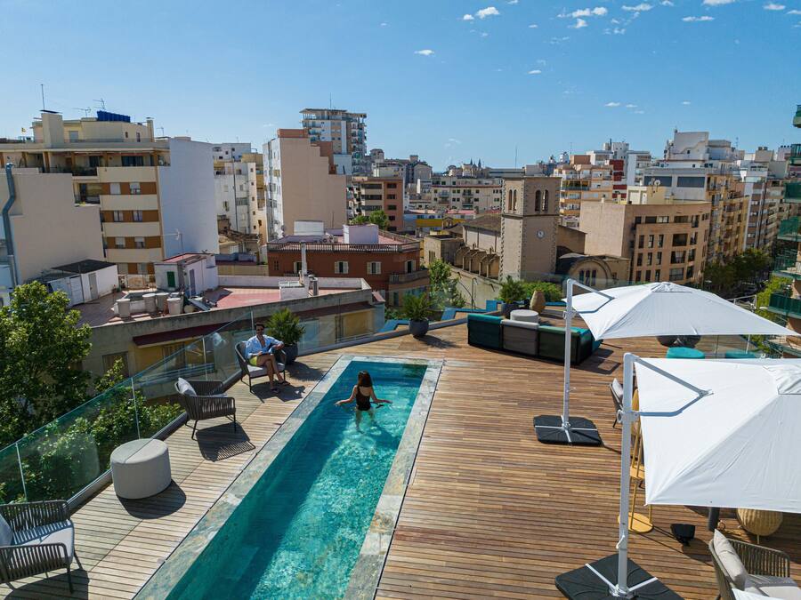 Una piscina en la azotea con cubierta de madera, sillones de descanso y sombrillas.