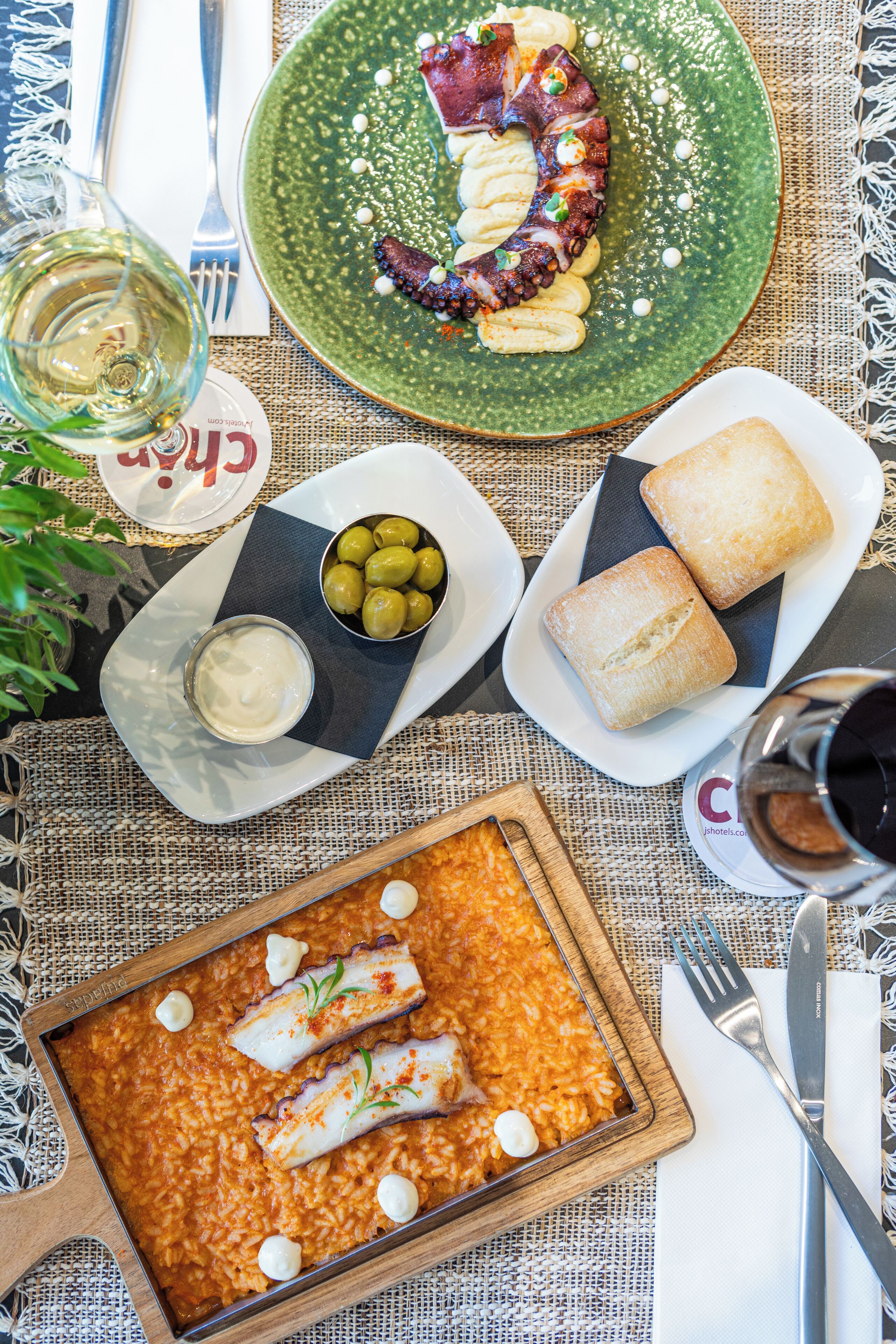 A dining table with a variety of dishes including octopus, olives, and pastries, along with wine glasses and cutlery.