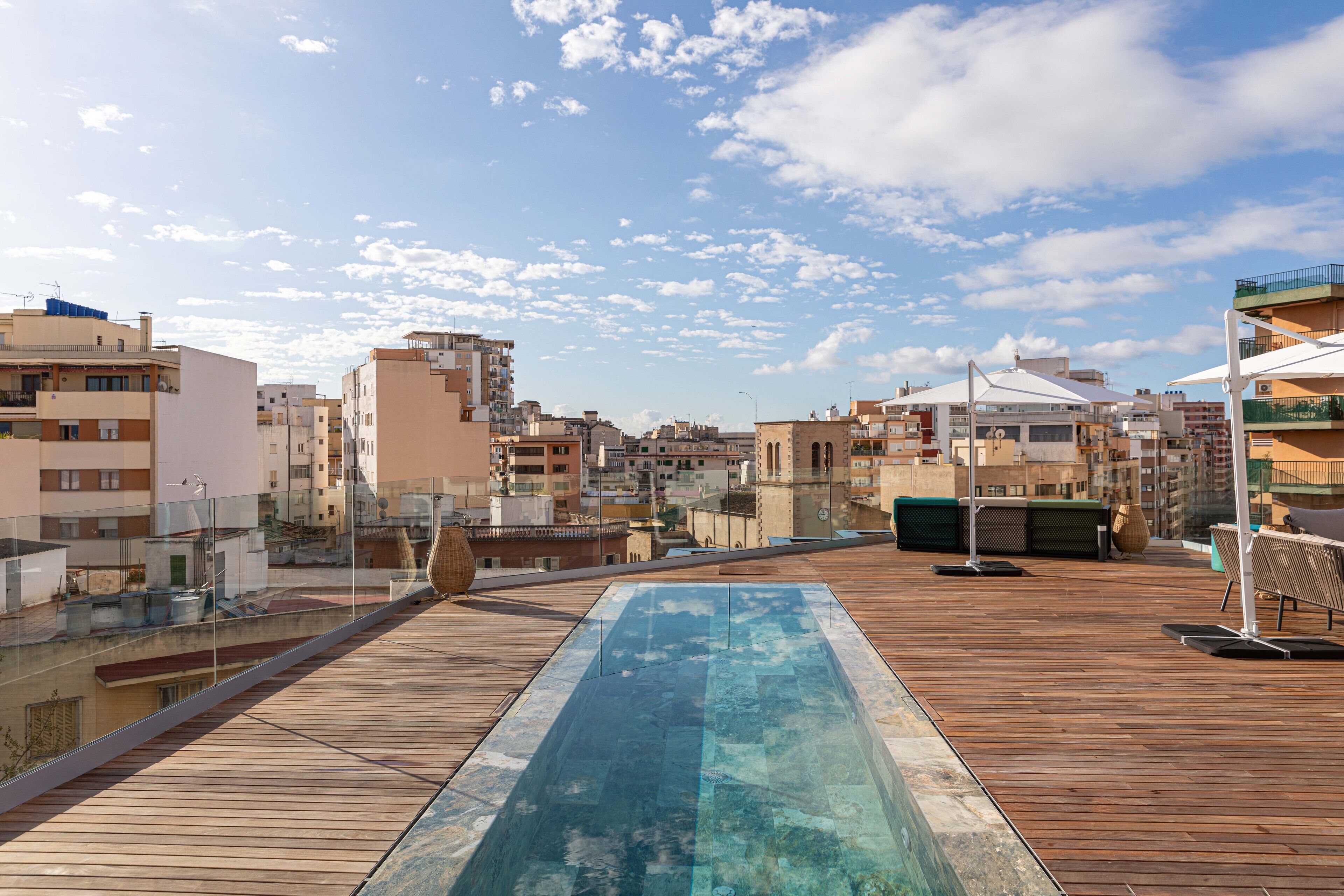 Piscina en la azotea con cubierta de madera, rodeada de edificios y cielo despejado.