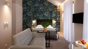 Una habitación de hotel moderna con una cama, un sofá, una mesita y un televisor montado en la pared.