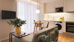 Una cocina moderna con microondas, horno y lavadora. Hay una mesa de comedor con sillas y una planta sobre una mesita auxiliar.