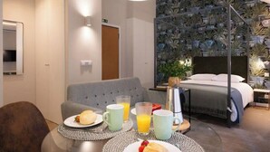 Una habitación de hotel con una cama, una mesa de desayuno y platos, vasos y una cafetera.