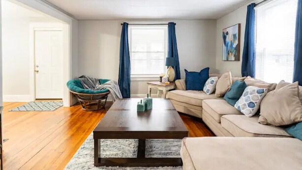 Un salon avec un plancher en bois, un canapé beige, une table basse foncée et un fauteuil vert.