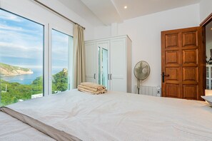 Une chambre avec un grand lit, une porte en bois, un ventilateur et une vue sur la mer.