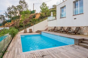 Une piscine dotée d’une terrasse en bois, entourée d’un mur de pierre et bordée d’une colline.