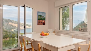 A dining area with a white table and chairs, a bowl of fruit, and a painting on the wall.