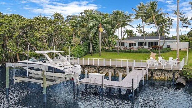 A dock with a boat, a house with a lawn, and palm trees. - Waterfront! Boat Dock and Guesthouse (North Palm Beach)